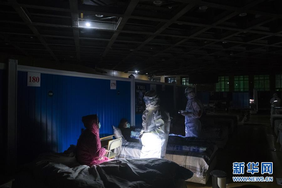 3月9日晚，在位于武汉市洪山体育馆的武昌方舱医院，江西支援湖北医疗队队员胡佩（右二）和杨成（右一）在熄灯后巡视。