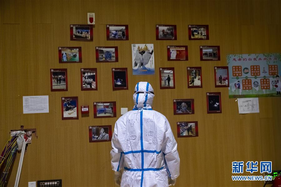3月9日晚，在武汉市洪山体育馆武昌方舱医院，名叫管茜的医务人员查看贴有该方舱里的新冠肺炎患者和医务人员照片的照片墙。