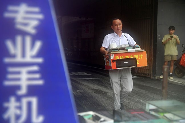 在江西省乐平市街头，程雪清抱着他的电脑和工具箱准备开始摆摊做生意，多年来，他一直从事手机贴膜的工作（7月7日摄）。新华社记者 彭昭之 摄