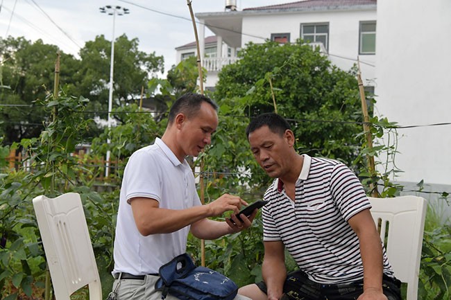 在江西省乐平市后港镇磻溪村，程雪清在抗美援朝烈士王来松的侄儿王光亮家中向他介绍寻访烈士墓地的过程，并将位于朝鲜开城的烈士墓地的照片给他看（7月6日摄）。新华社记者 彭昭之 摄