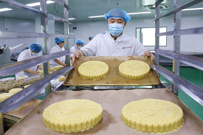 9月13日，在山东省青岛西海岸新区一家月饼生产企业，工人将制作好的大月饼放到烤架上。新华社发（王培珂摄）